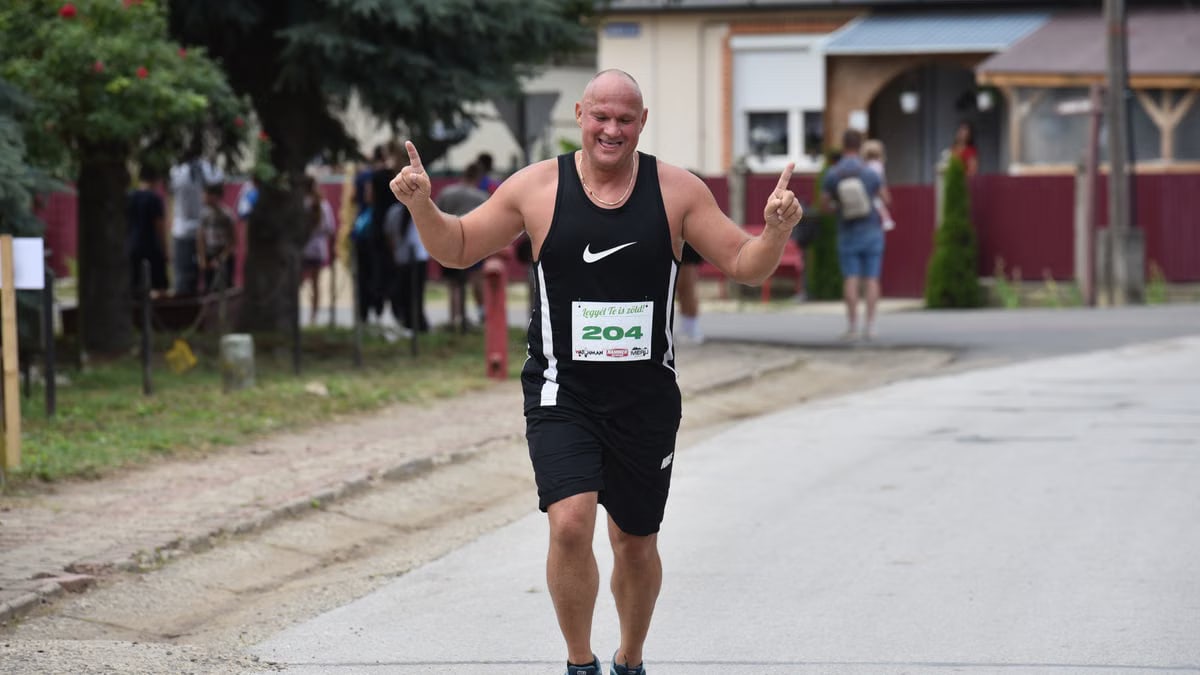 Joyful runner at a race finish line outdoors, raising arms in celebration.