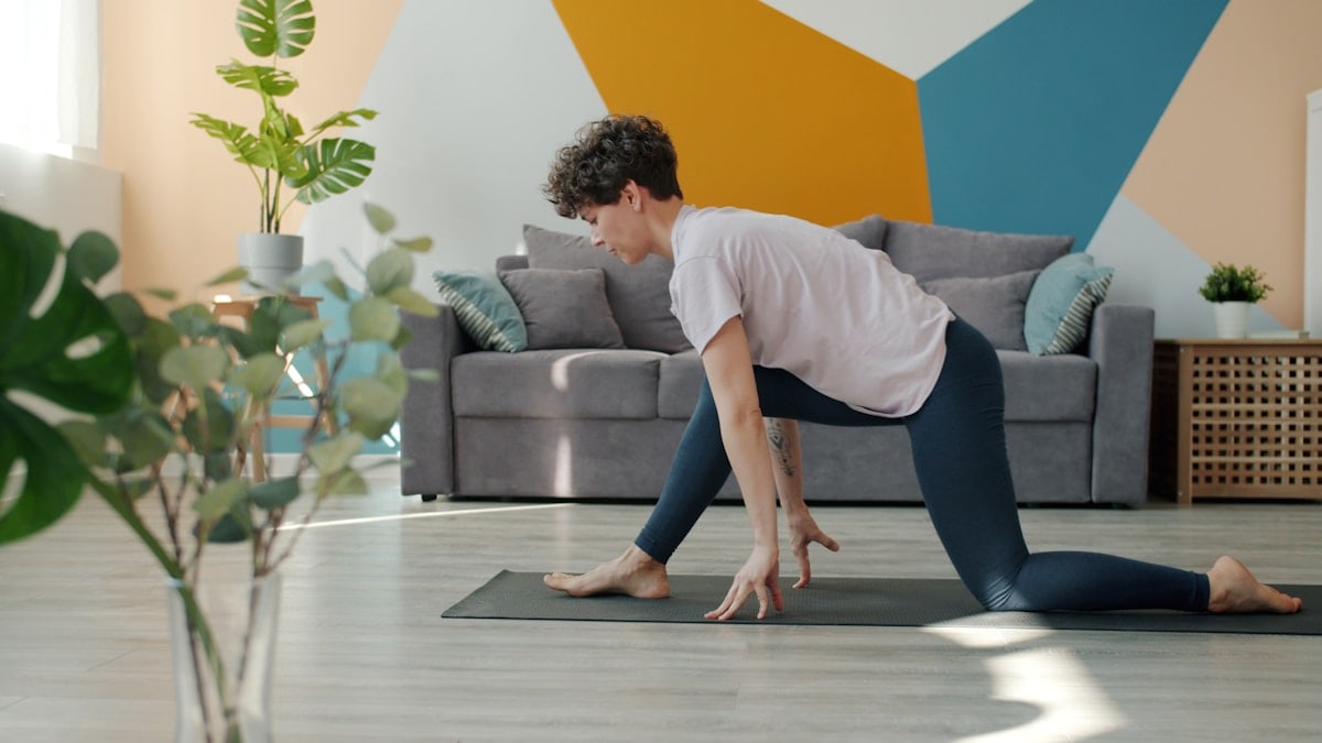 Flexible young woman is doing yoga in house practising asanas alone on comfy mat enjoying useful activity. Indoor sports, active lifestyle and modern youth concept.